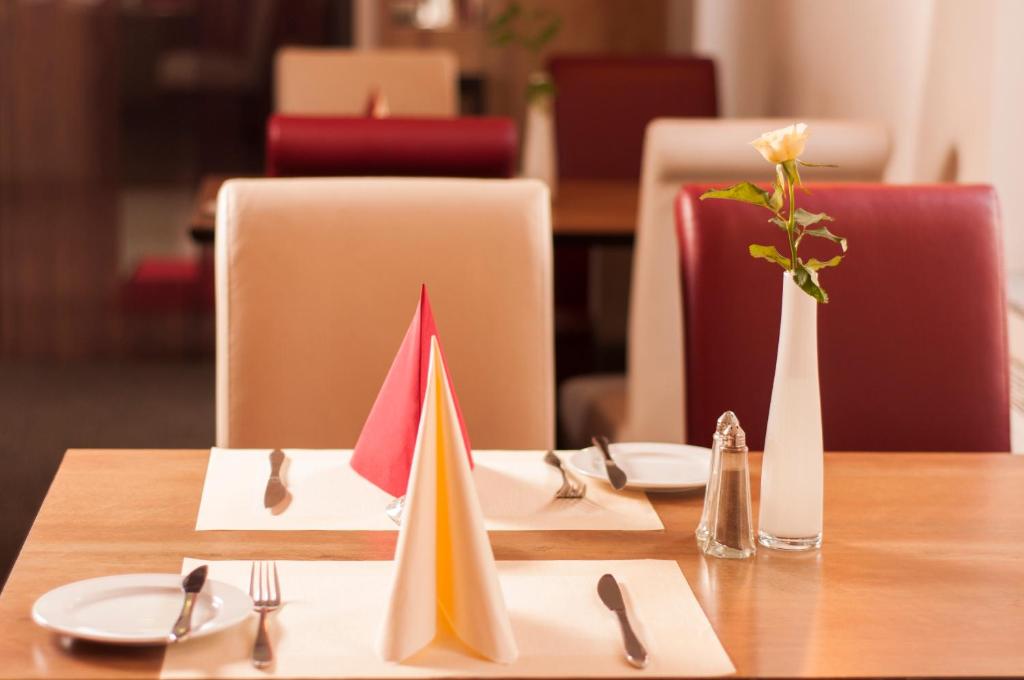 einen Holztisch mit Tellern und Servietten und eine Vase mit einer Blume in der Unterkunft Hotel Dietrichsdorfer Hof in Kiel