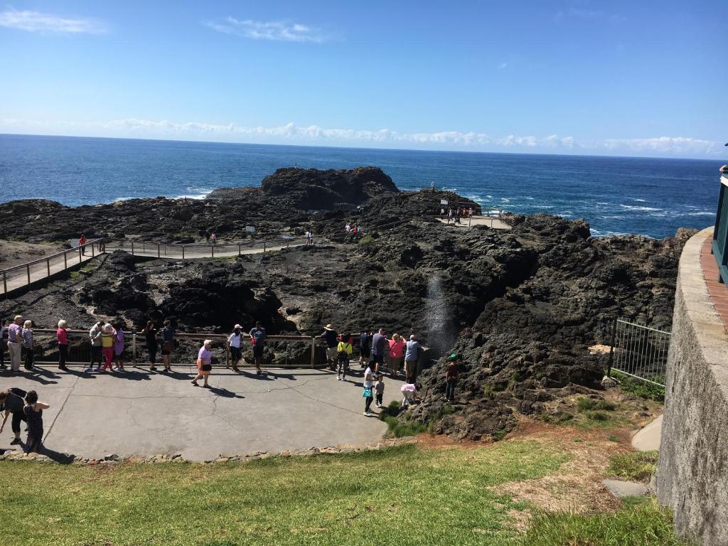 um grupo de pessoas em pé em um penhasco perto do oceano em Sea Whispers em Kiama