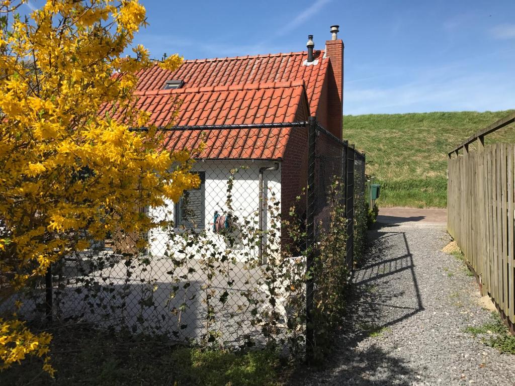 uma casa com um telhado vermelho e uma cerca em Heerlijk Dijkhuisje in Paal em Graauw