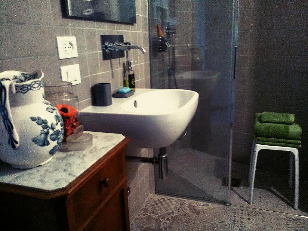 y baño con lavabo y ducha con mampara de cristal. en Oddi21 B&B, en Albenga