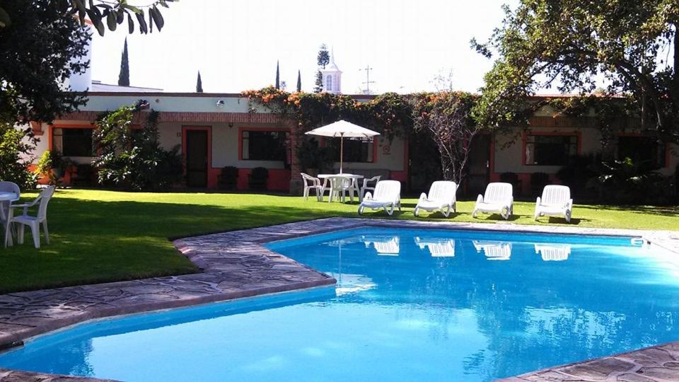 een zwembad met stoelen, een tafel en een parasol bij Hotel Los Mezquites in Tequisquiapan