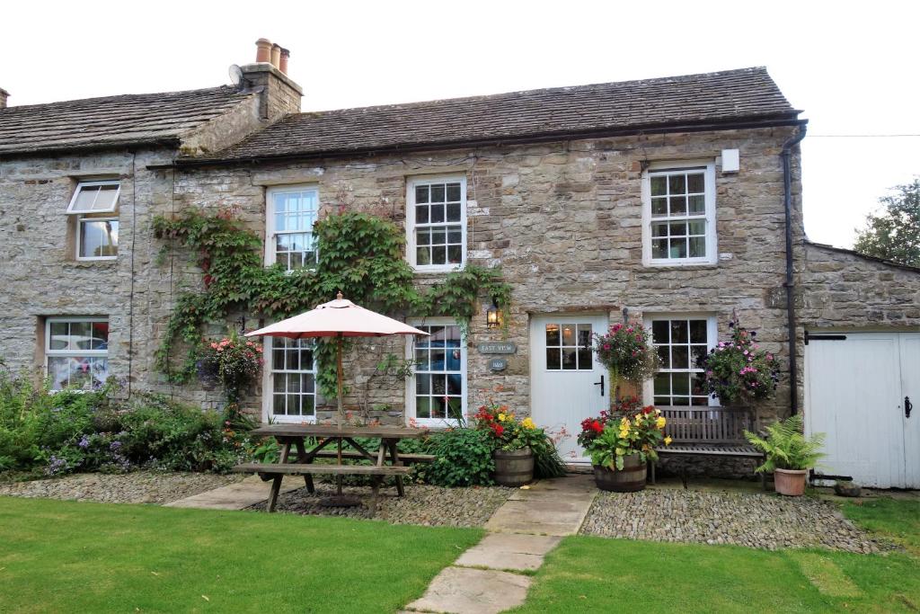 an old stone house with a table and an umbrella at Eastview Bed and Breakfast in Garrigill