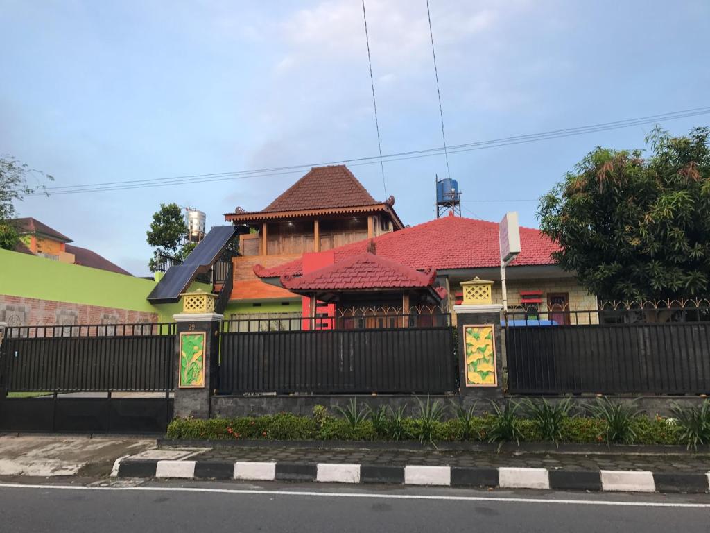 Jogja Classic Homestay Syariah في يوغياكارتا: منزل بسقف احمر وسياج اسود