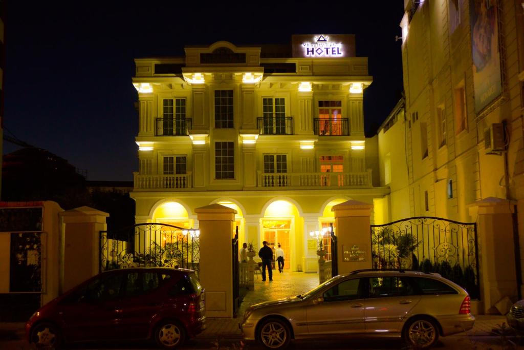 two cars parked in front of a building at night at Hotel Vila Imperial in Elbasan