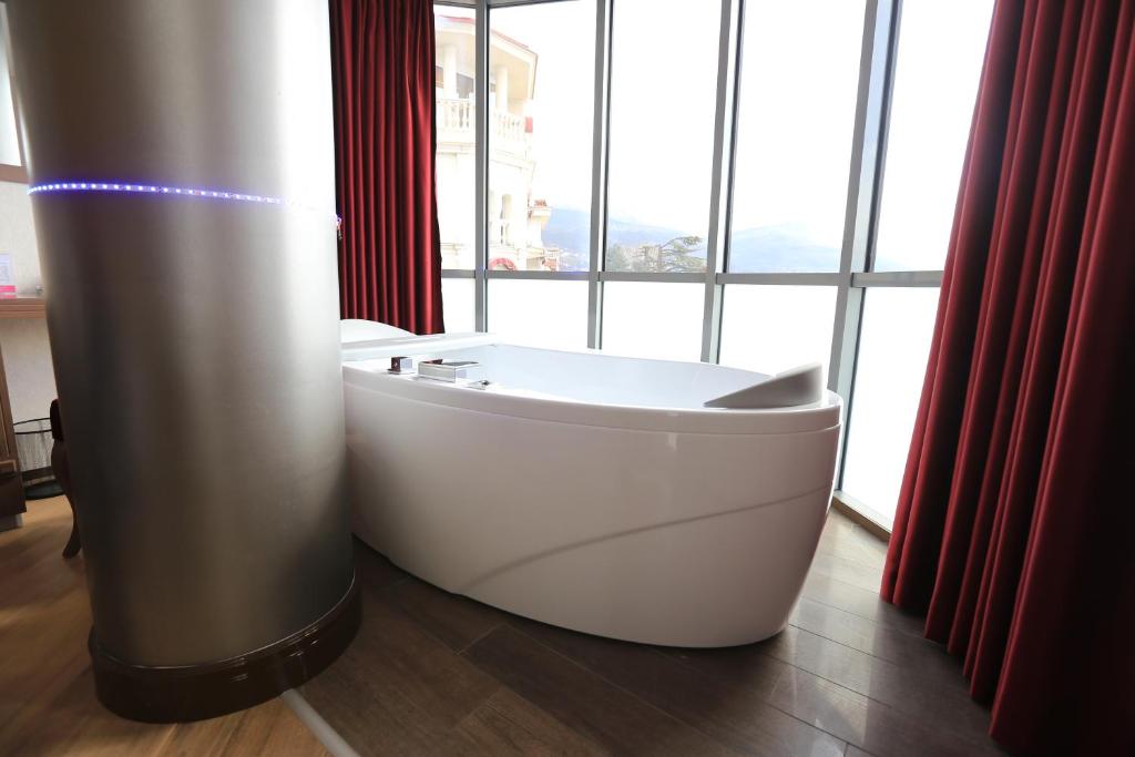 Corner bathtub with LED column and floor-to-ceiling windows with red curtains and mountain view at City Palace Hotel in Ohrid