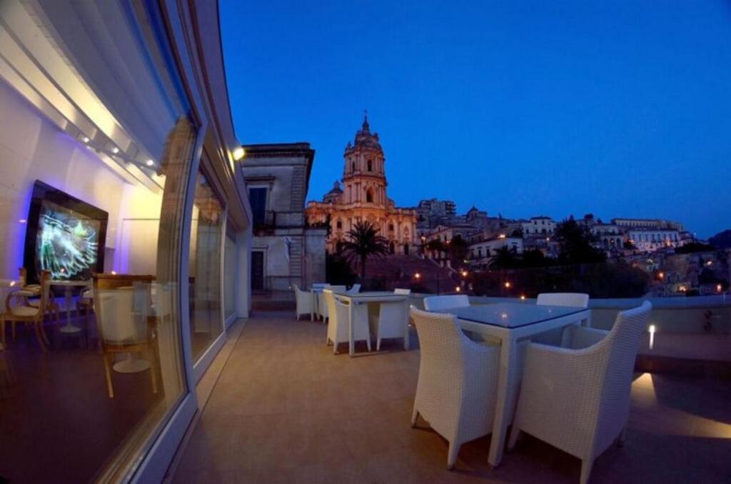 a balcony with white tables and white chairs at night at San Giorgio Modica Hotel in Modica