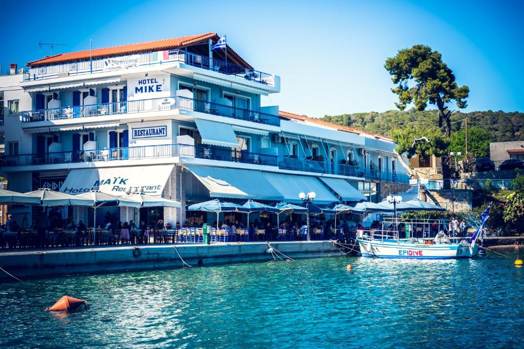 a large white building next to the water with a boat at Hotel Mike in Ancient Epidauros