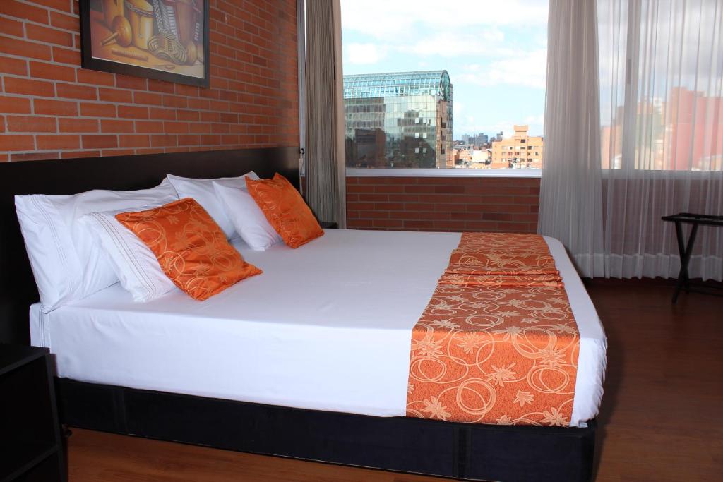 a bedroom with a bed with orange pillows and a window at Hotel Bogota Astral in Bogotá