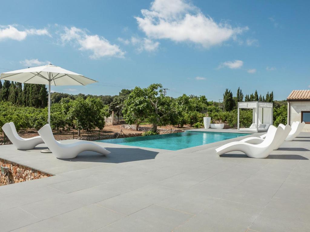 a swimming pool with white chairs and an umbrella at Belvilla by OYO Calet in Muro