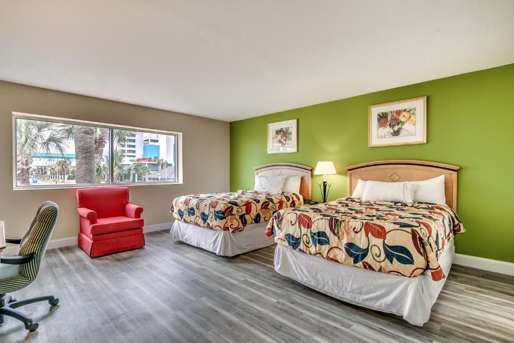 two beds in a room with green walls and a red chair at Beachcomber Inn & Suites in Myrtle Beach