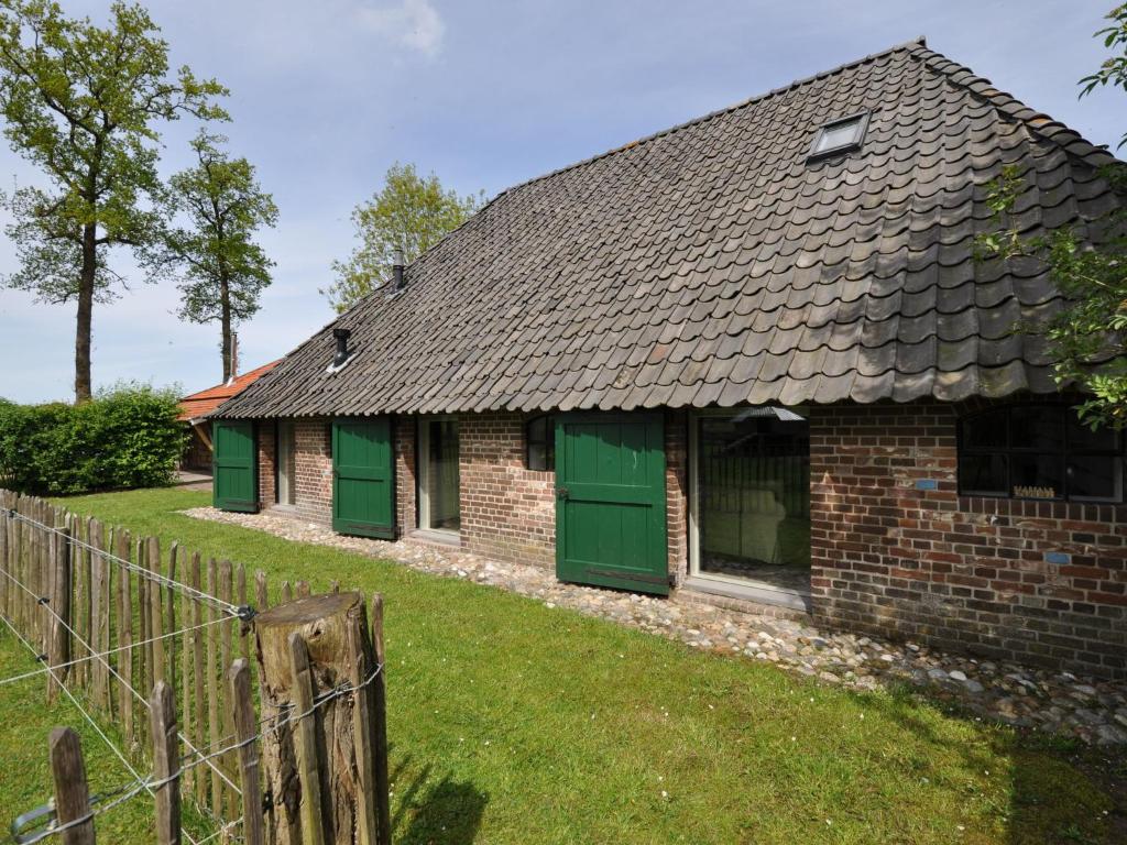 uma velha casa de tijolos com portas verdes e uma cerca em Stylish Farmhouse in Nieuwleusen with Private Garden and Sauna em Nieuwleusen