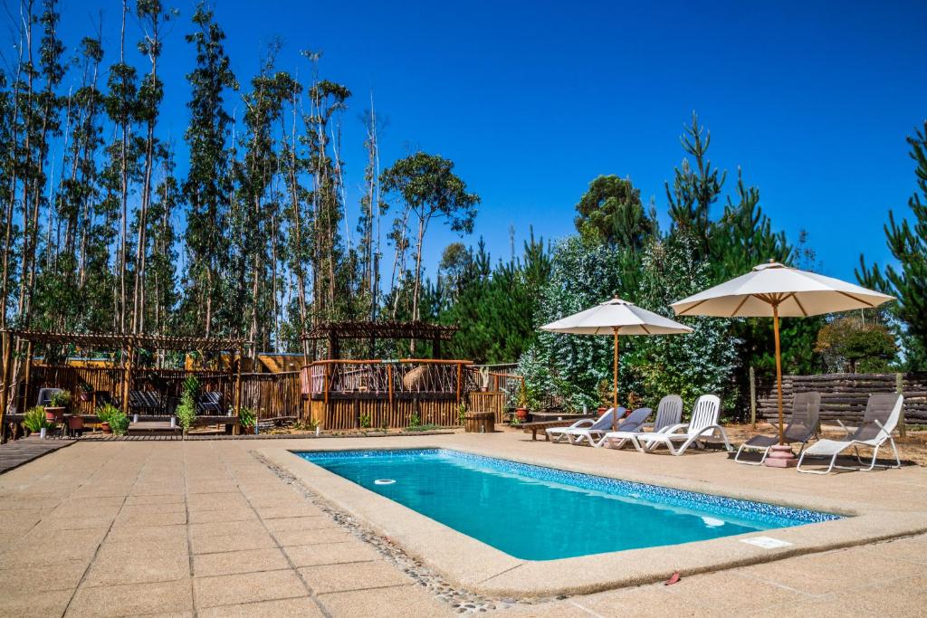 a swimming pool with two chairs and umbrellas at El Bosque Lodge in Algarrobo