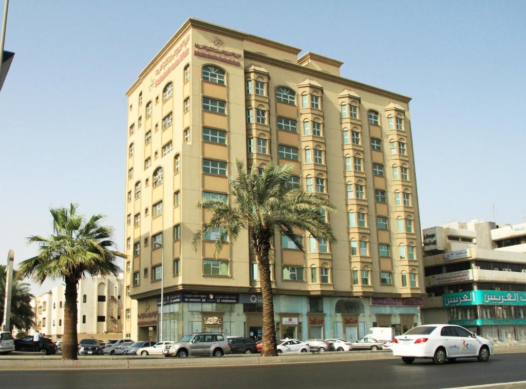 a large building with palm trees in front of a street at Al Rabitah Al Fondoqeiah Hotel Apartments in Jeddah