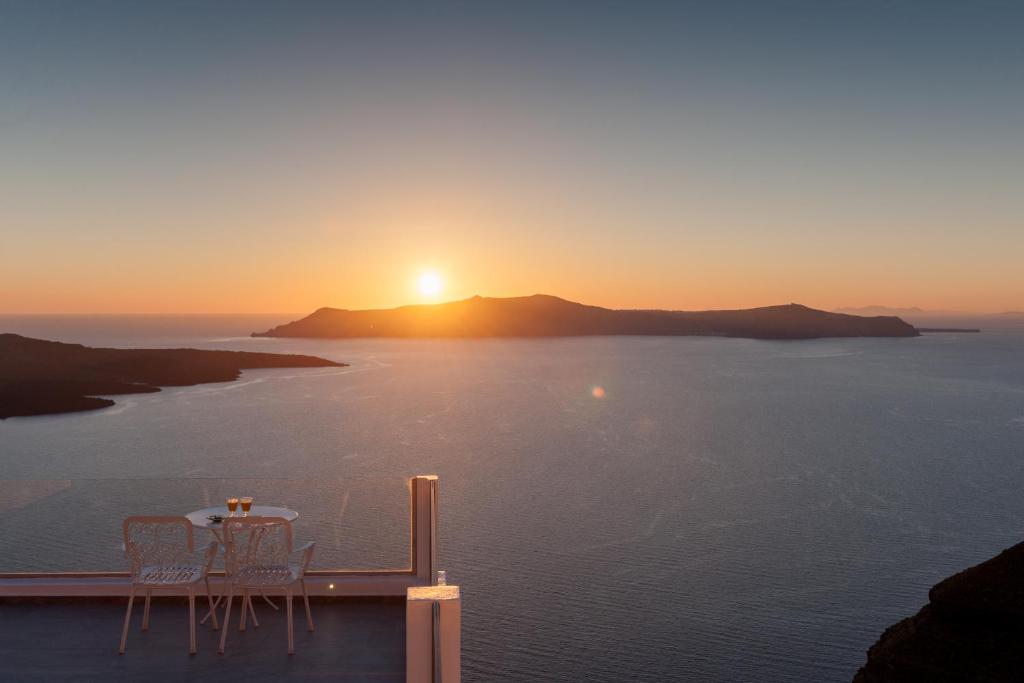 a table and chairs on a balcony with the sunset at Villa Renos Hotel in Fira