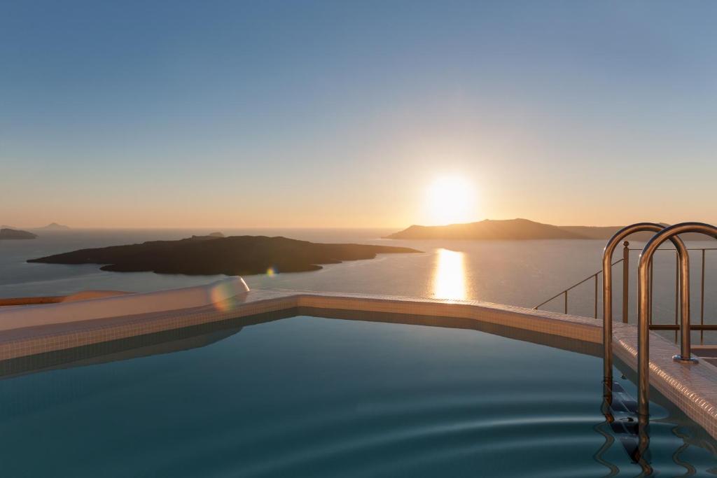 a infinity pool with a view of the ocean at sunset at Villa Renos Hotel in Fira