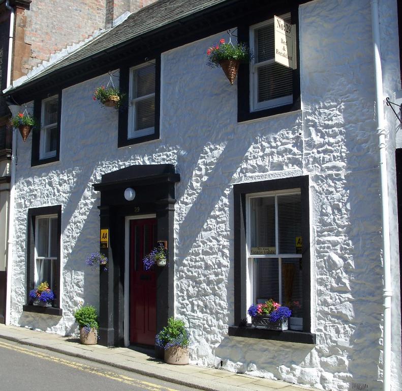 a white building with plants on the windows and a red door at 29 Well Street B&B in Moffat