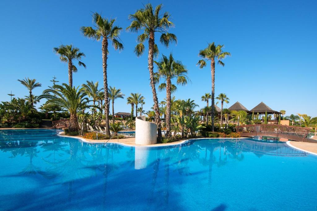 a large swimming pool with palm trees in the background at Puerto Antilla Grand Hotel in Islantilla
