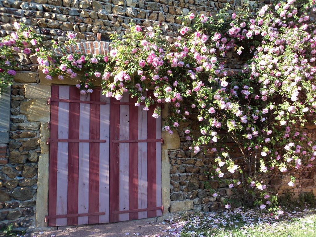 a brick wall with a red door with pink flowers at Chambres d'Hôtes La Vie en Roses in Iguerande