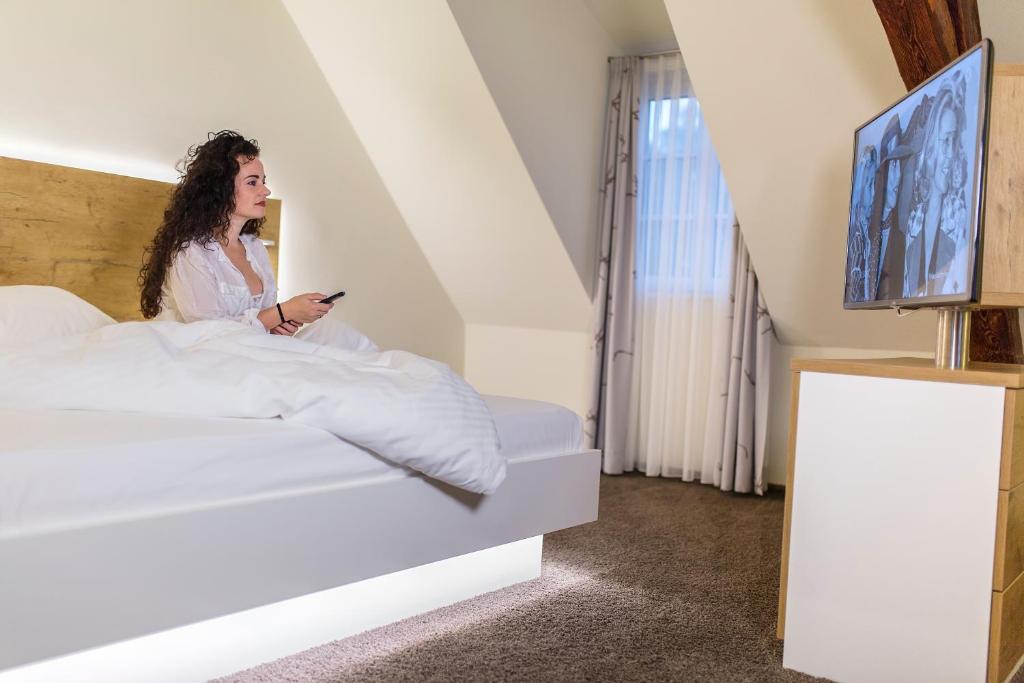 une femme assise au lit en regardant son téléphone portable dans l'établissement Hotel Jägerhaus in Esslingen, à Esslingen am Neckar