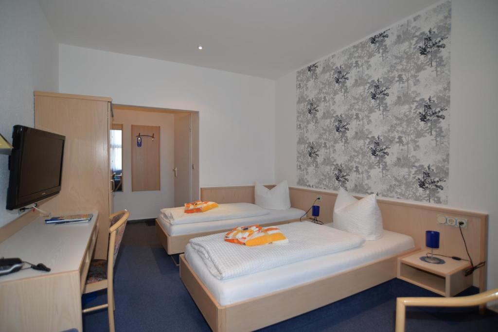 a room with two beds and a desk and a tv at Hotel Am Hohen Schwarm in Saalfeld