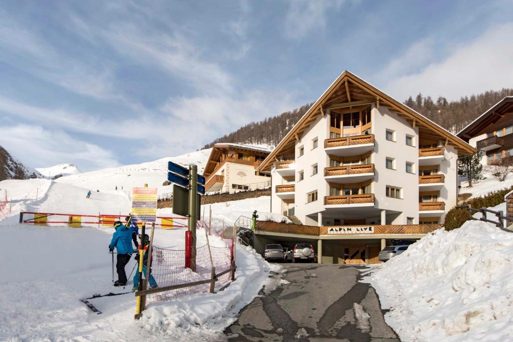 duas pessoas de pé na neve em frente a um alojamento de esqui em Appartements Garni Alpin Live em Samnaun