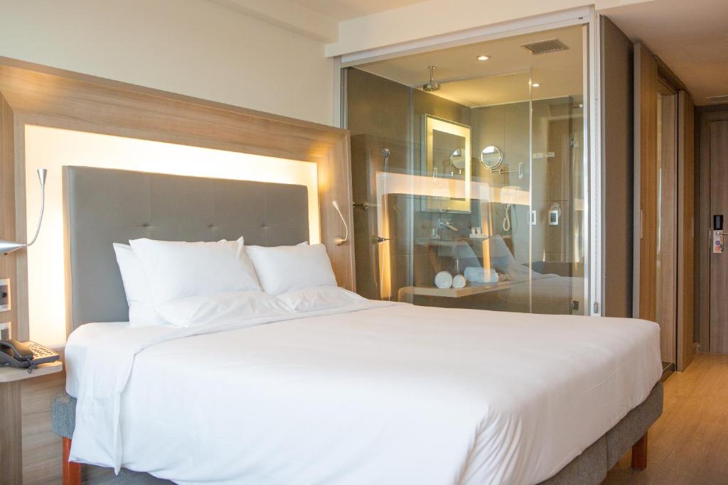 a bedroom with a large white bed and a glass wall at Novotel RJ Porto Atlantico in Rio de Janeiro