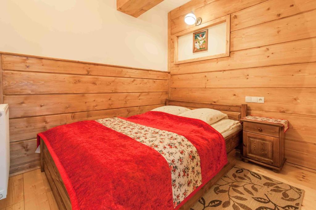 - une chambre avec des murs en bois et un lit avec une couverture rouge dans l'établissement Willa "Zosia ", à Zakopane