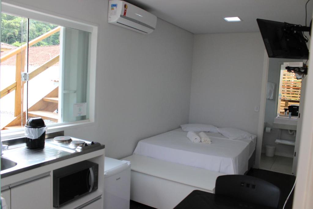 um pequeno quarto branco com uma cama e uma janela em Praia Camburi - Studios Kuta em Camburi