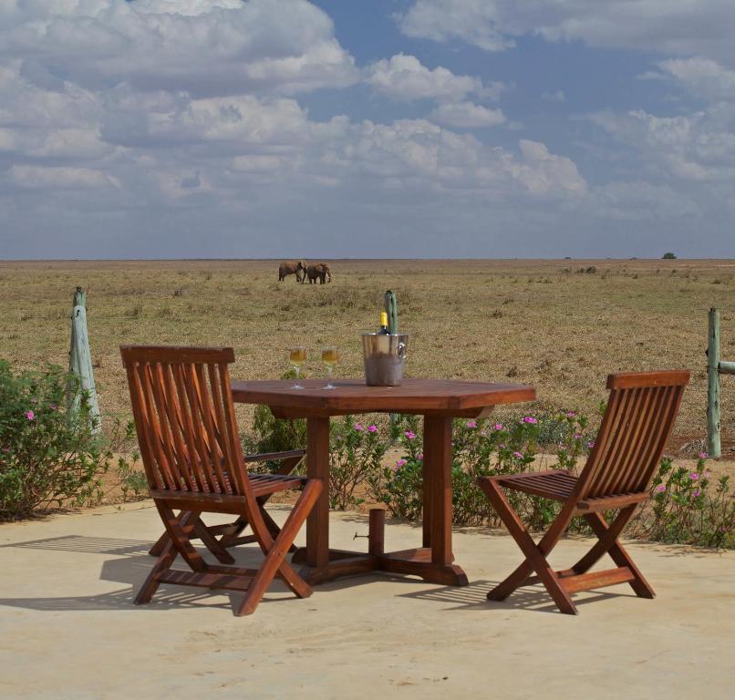a picnic table with two chairs and a horse in the field at Ashnil Aruba Lodge in Tsavo