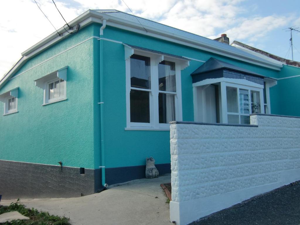 una casa azul con un gato sentado frente a ella en Oamaru Green Cottage, en Oamaru