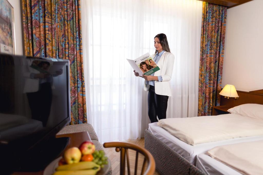 una mujer parada en una habitación de hotel con un libro en Komfort-Hotel Stockinger, en Linz