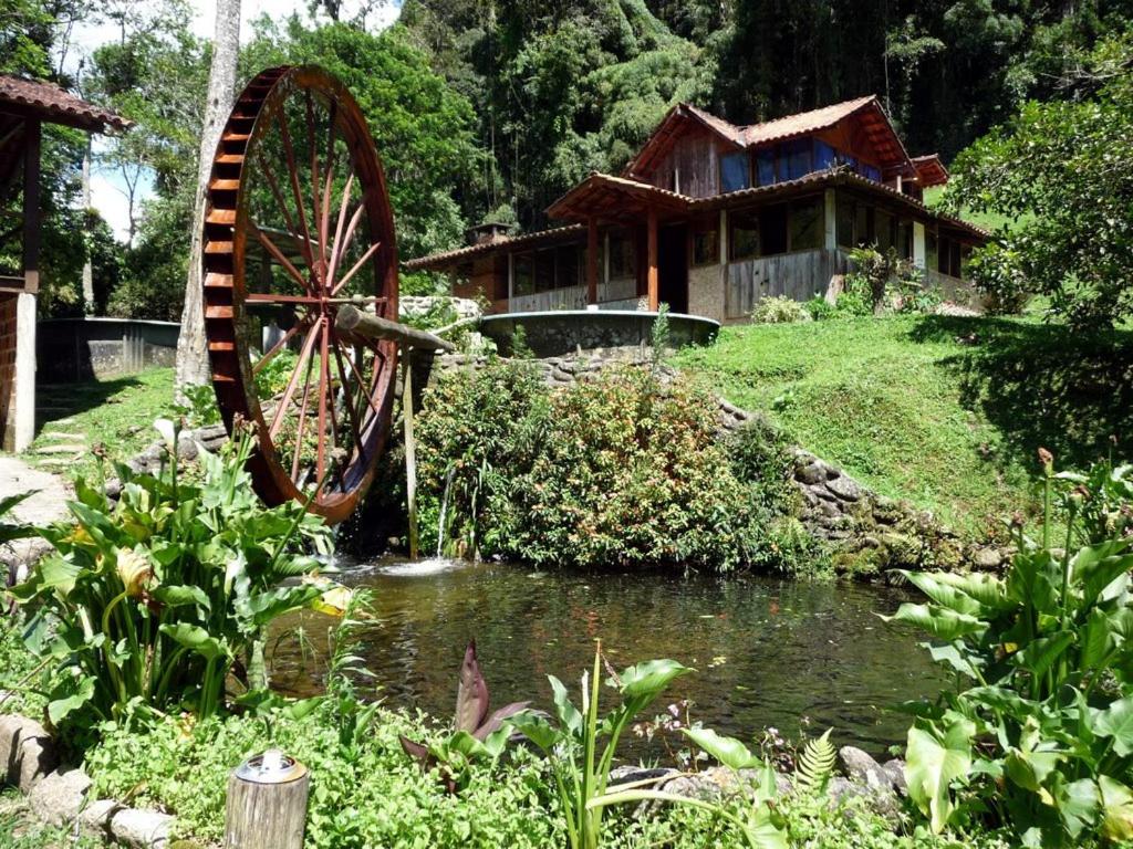 ein Wasserrad vor einem Haus mit einem Teich in der Unterkunft Chalé Truta da Floresta in Visconde De Maua