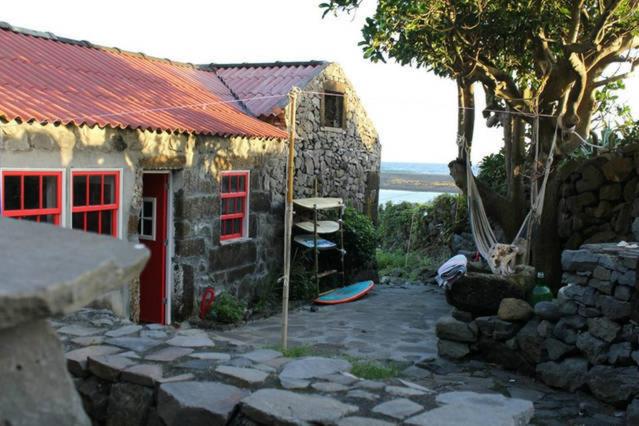 a stone house with a red door and a rock yard at Casa da Lagoa AL 416 in Fajã da Caldeira de Santo Cristo