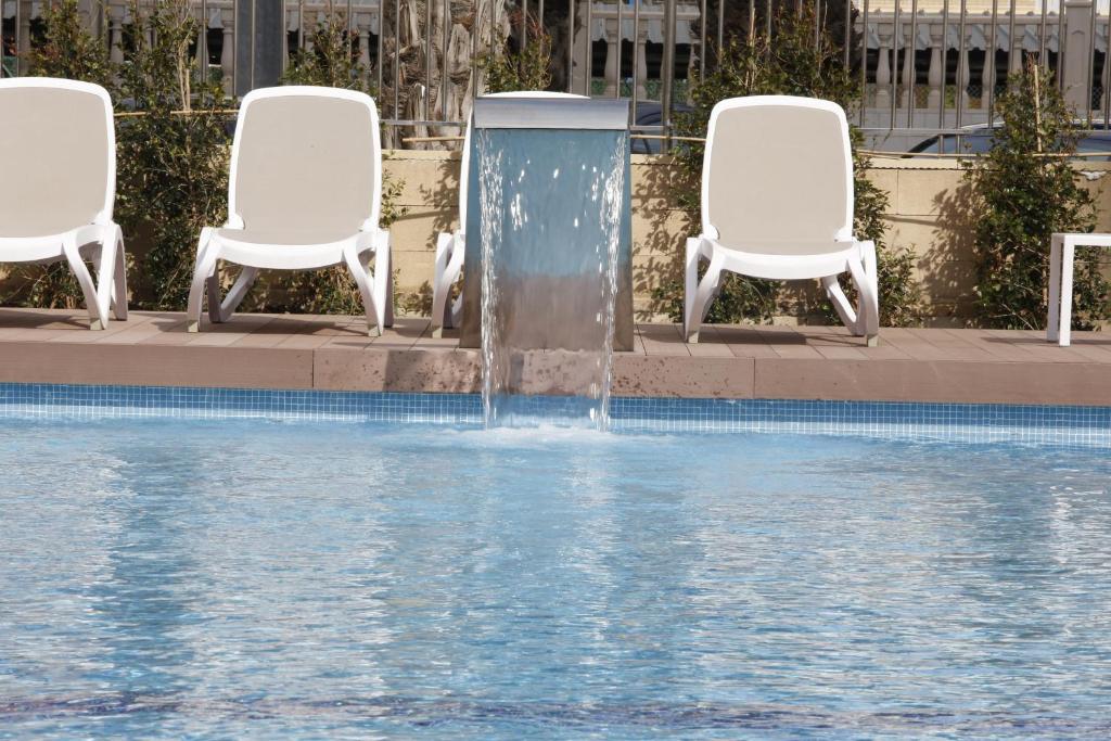 two white chairs and a fountain in a pool at Hotel Castilla Alicante in Alicante