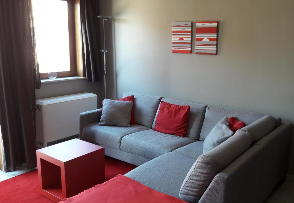 uma sala de estar com um sofá cinzento e almofadas vermelhas em Appartement Duinenzicht De Haan-Vosseslag em De Haan