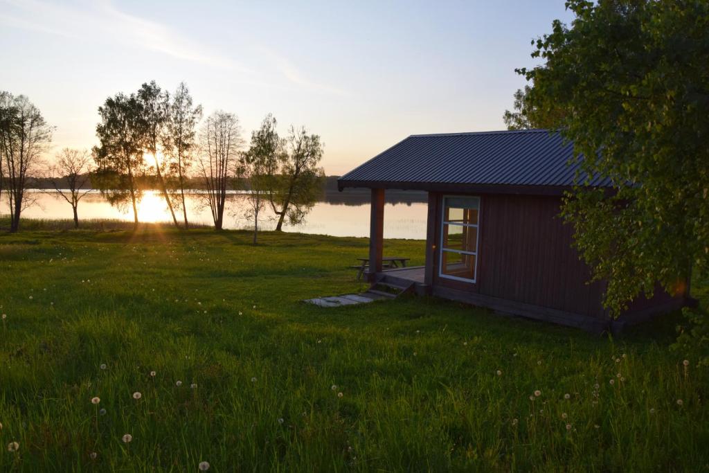 a small cabin in a grassy field with the sunset at Lāde in Lādezers