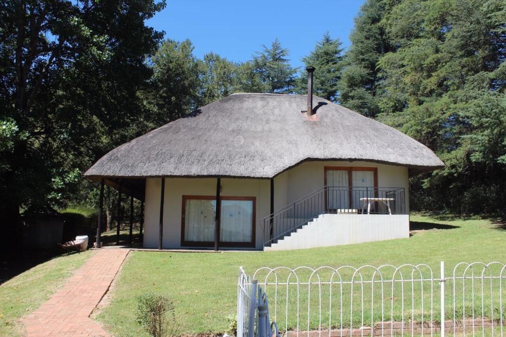 a small hut with a grass roof on a field at Lairds Lodge in Underberg