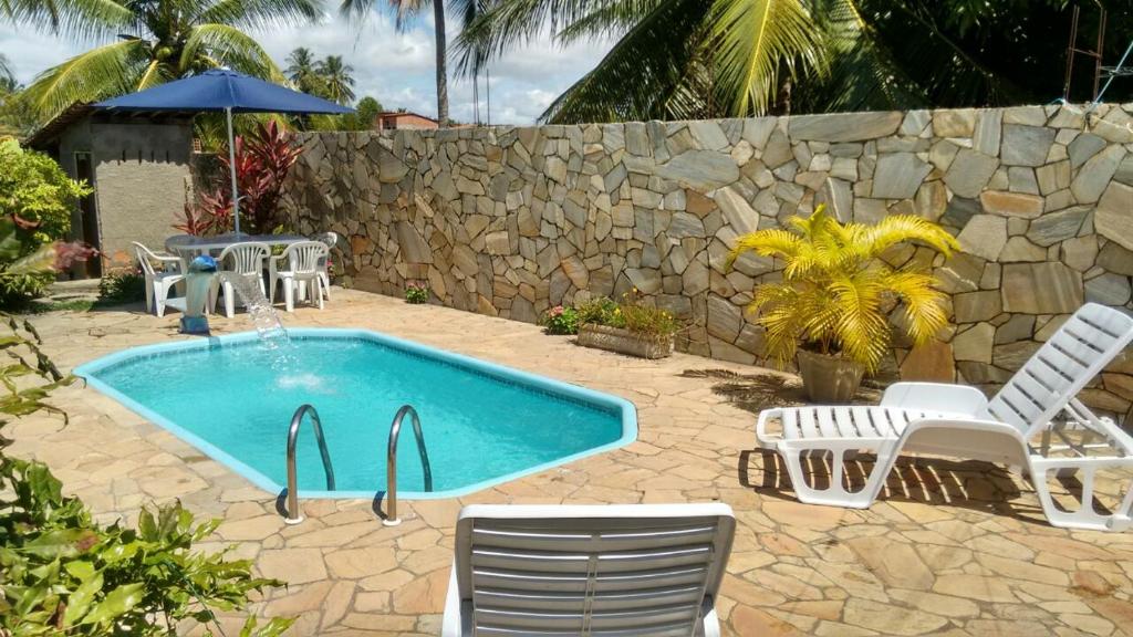 a swimming pool with chairs and a stone wall at Casa Caiçara in São Miguel dos Milagres