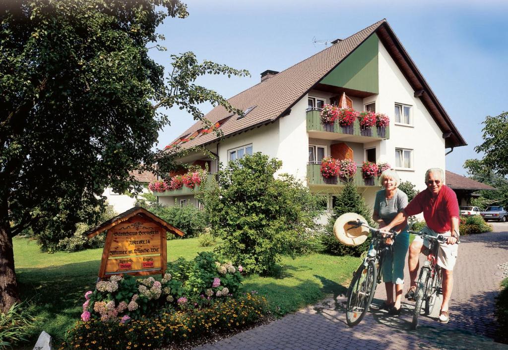 Ein Mann und eine Frau auf einem Fahrrad vor einem Haus in der Unterkunft Gästehaus Hornstein in Nonnenhorn