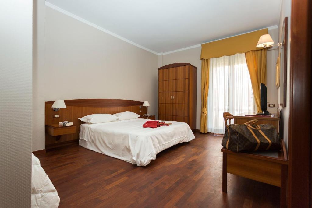a bedroom with a white bed and wooden floors at Hotel Cavaliere in Noci