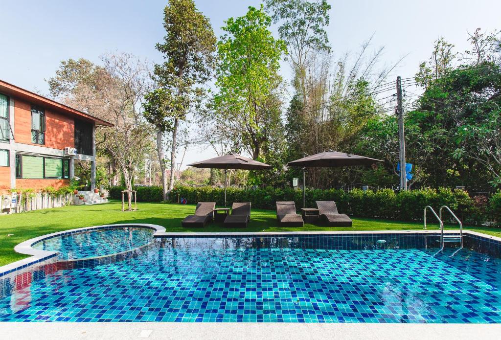 a swimming pool with chairs and umbrellas in a yard at Stucco Loft Residency in Chiang Mai