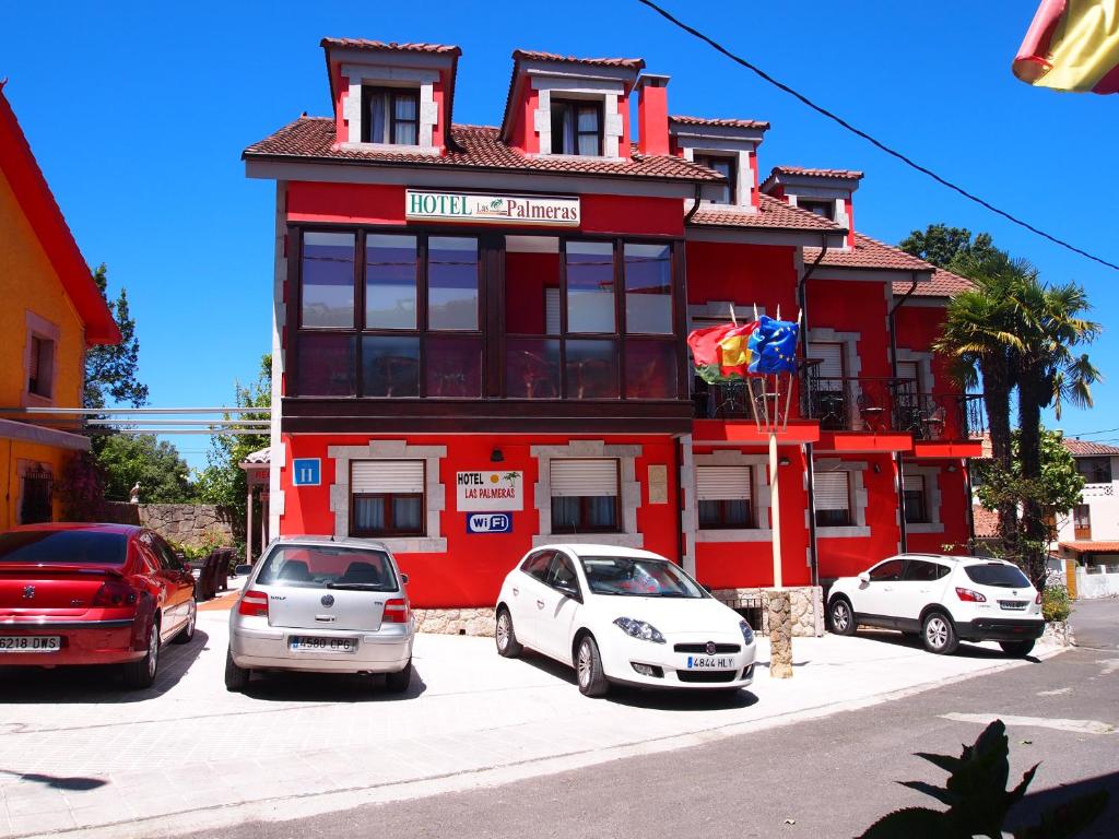 a red building with cars parked in front of it at Hotel Las Palmeras Celorio in Llanes