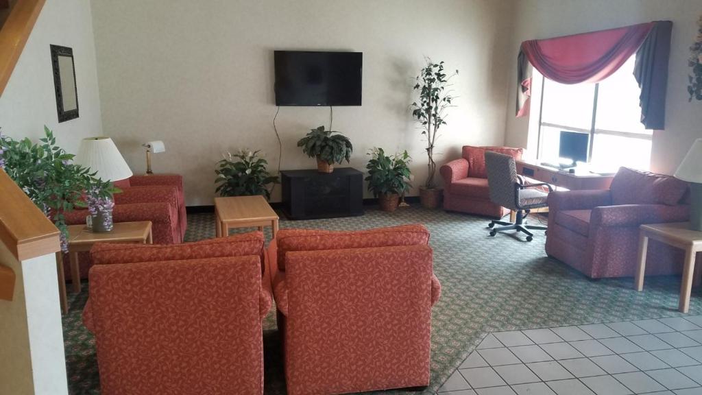 a living room with red chairs and a tv at Syracuse Inn and Suites in Syracuse