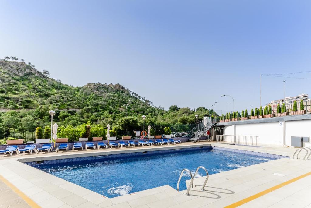 une piscine avec des chaises bleues et une montagne dans l'établissement Hotel Maya Alicante, à Alicante