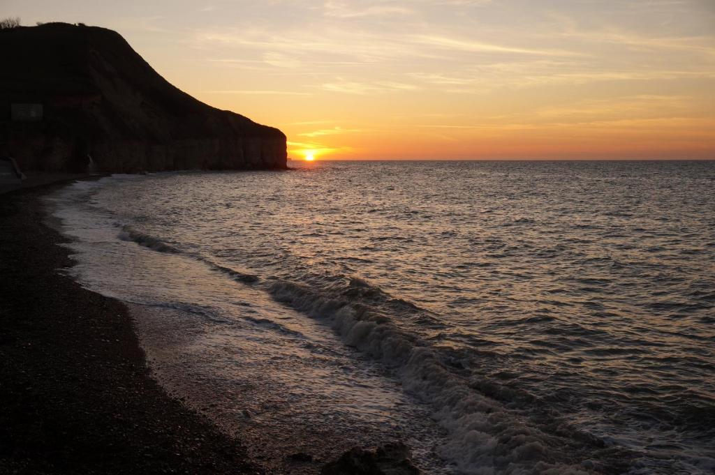 a sunset over the ocean with a rocky beach at Le Clos Saint Jean in Sainte-Honorine-des-Pertes