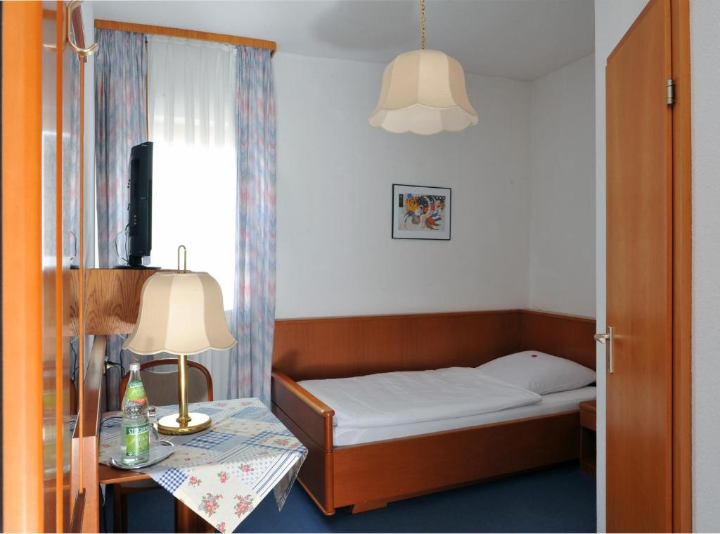 a small bedroom with a bed and a table with a lamp at Hotel Grüner Baum in Pommersfelden