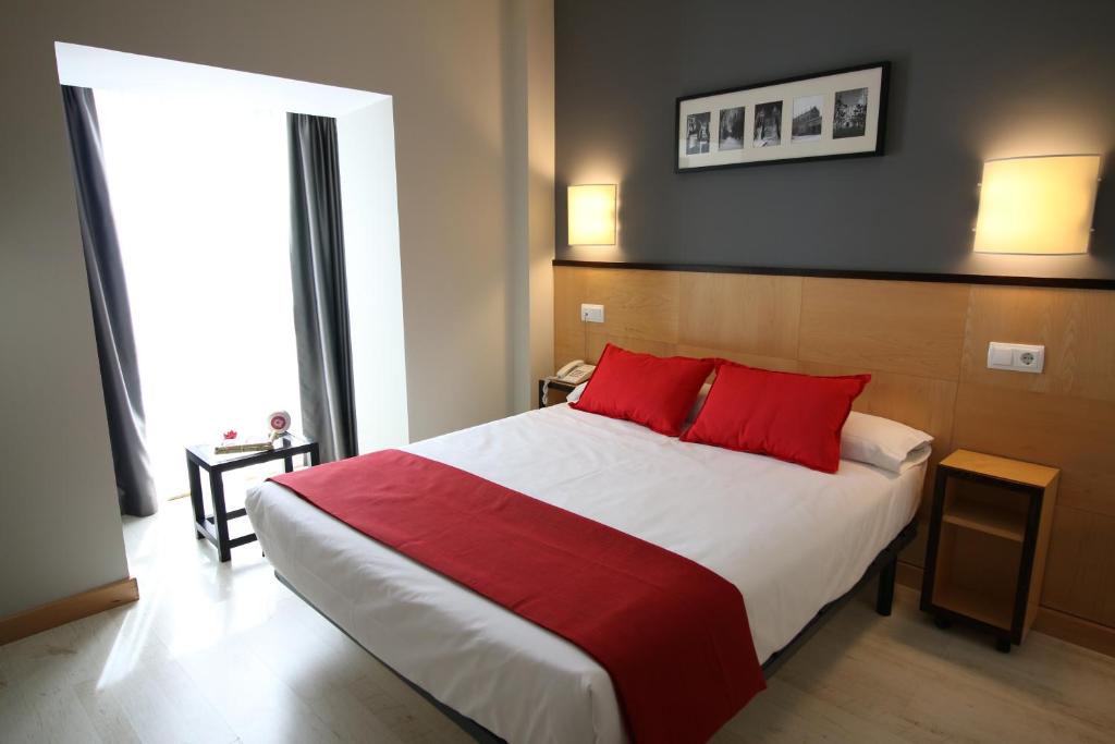 a bedroom with a large bed with red pillows at Hotel Alda Entrearcos in Burgos