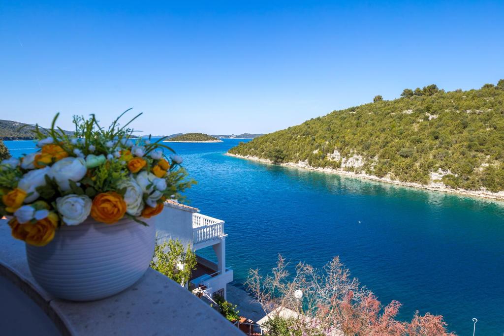 eine Vase voller Blumen auf einem Felsvorsprung neben dem Wasser in der Unterkunft Vidučić Apartments in Dragove