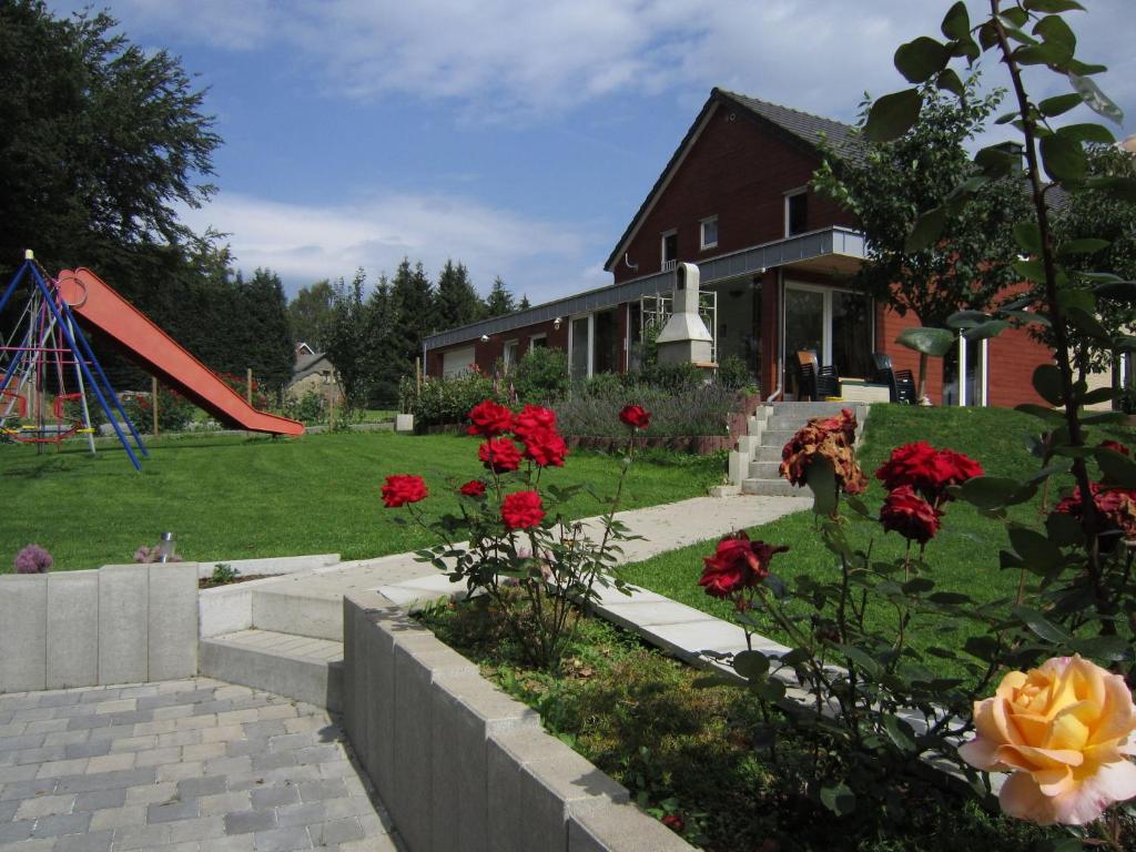ein Haus mit einem Garten mit roten Blumen und einem Spielplatz in der Unterkunft Cozy Holiday Home in Robertville with Sauna in Robertville