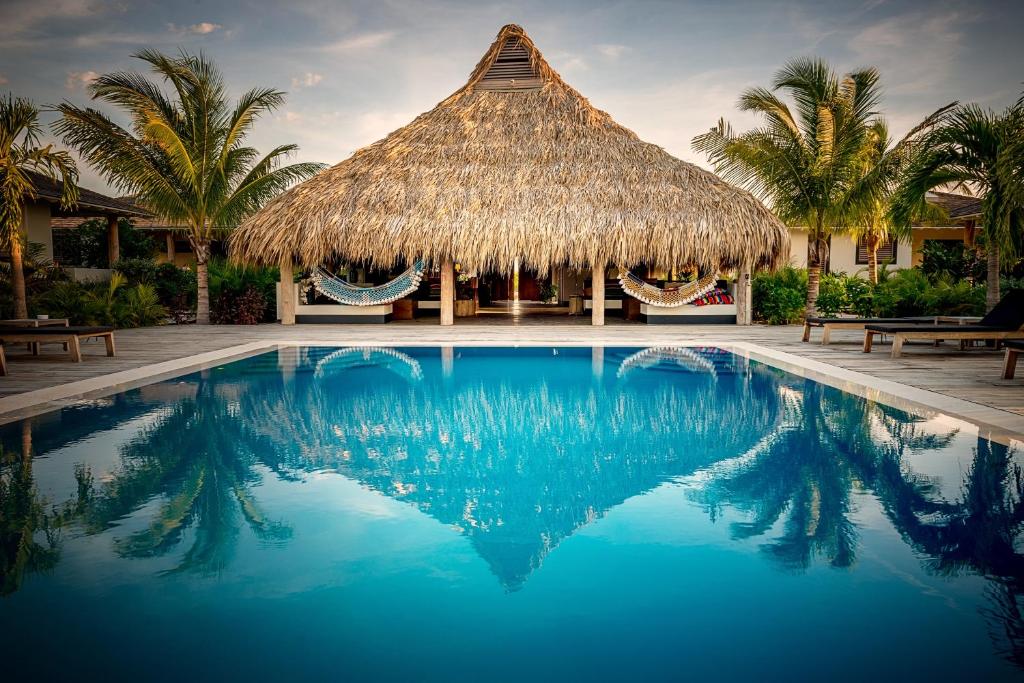 uma piscina de resort com uma cabana de palha e palmeiras em Windhoek Resort Bonaire em Kralendijk